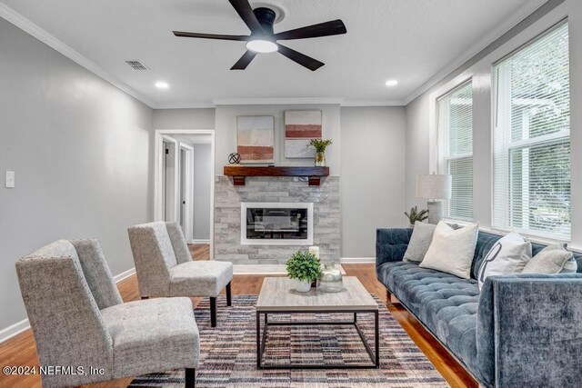 living room with ceiling fan, hardwood / wood-style floors, a stone fireplace, and ornamental molding