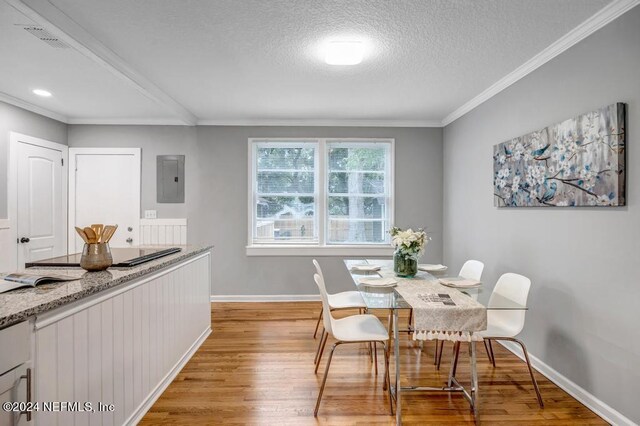 dining room with light hardwood / wood-style floors, ornamental molding, a textured ceiling, and electric panel