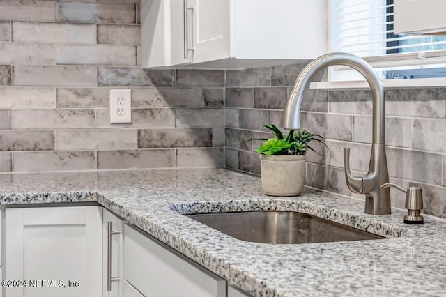 room details with light stone countertops, sink, white cabinets, and backsplash