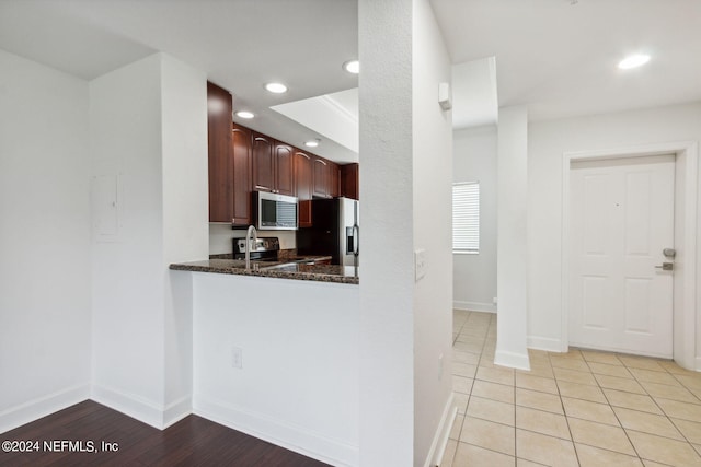 kitchen with appliances with stainless steel finishes, light hardwood / wood-style flooring, and dark stone countertops