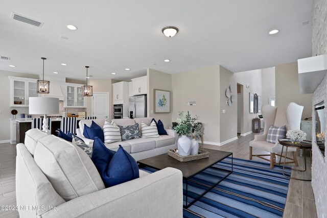 living room with light wood-style flooring, visible vents, baseboards, and recessed lighting