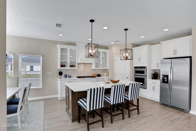 kitchen with a center island, white cabinets, appliances with stainless steel finishes, decorative light fixtures, and light hardwood / wood-style floors