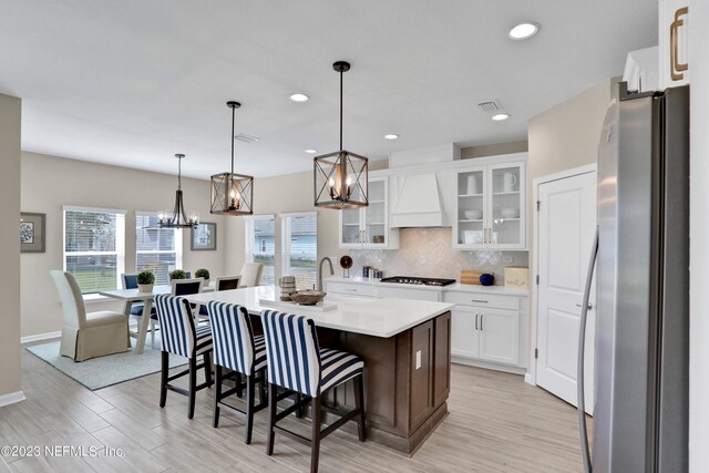 kitchen with gas stovetop, light countertops, freestanding refrigerator, tasteful backsplash, and custom range hood