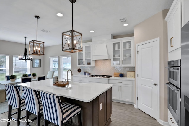 kitchen with white cabinets, an island with sink, decorative light fixtures, custom range hood, and gas cooktop