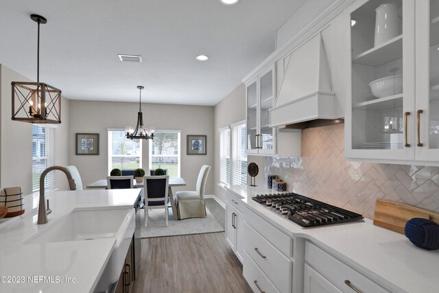 kitchen with stainless steel gas stovetop, custom exhaust hood, light hardwood / wood-style flooring, white cabinets, and hanging light fixtures