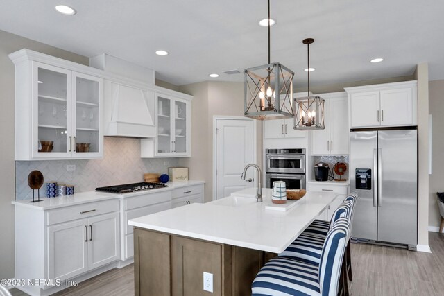 kitchen featuring pendant lighting, premium range hood, sink, an island with sink, and appliances with stainless steel finishes