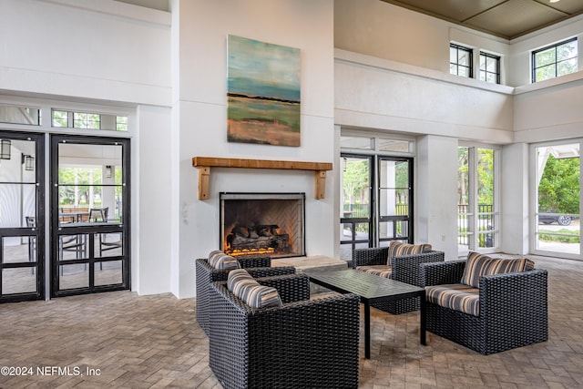 living room with brick floor, a healthy amount of sunlight, a fireplace with raised hearth, and a high ceiling