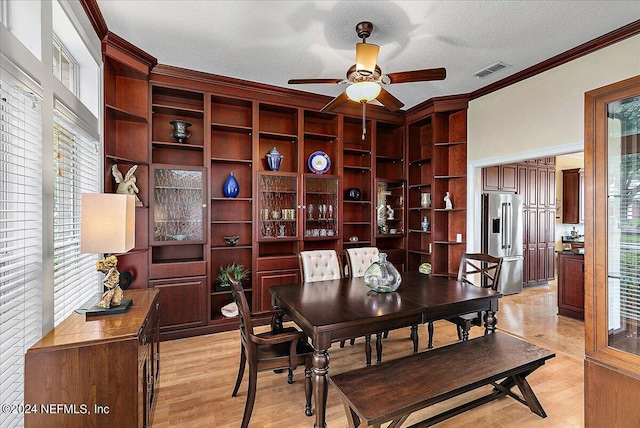 dining room featuring a textured ceiling, light wood-style flooring, a ceiling fan, visible vents, and crown molding