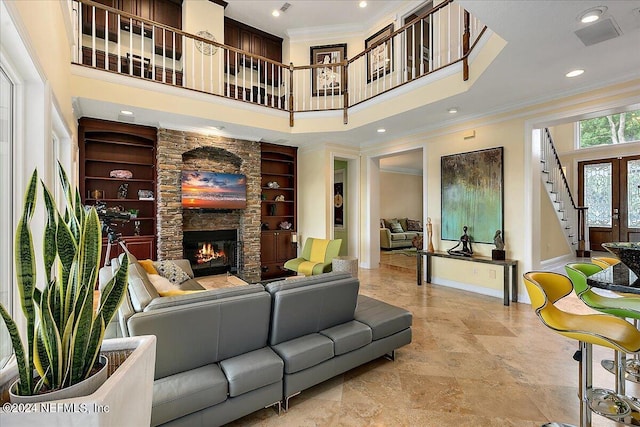 living room featuring baseboards, built in features, ornamental molding, a high ceiling, and a stone fireplace