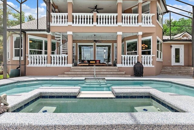 rear view of property featuring a balcony, glass enclosure, a pool with connected hot tub, and a ceiling fan