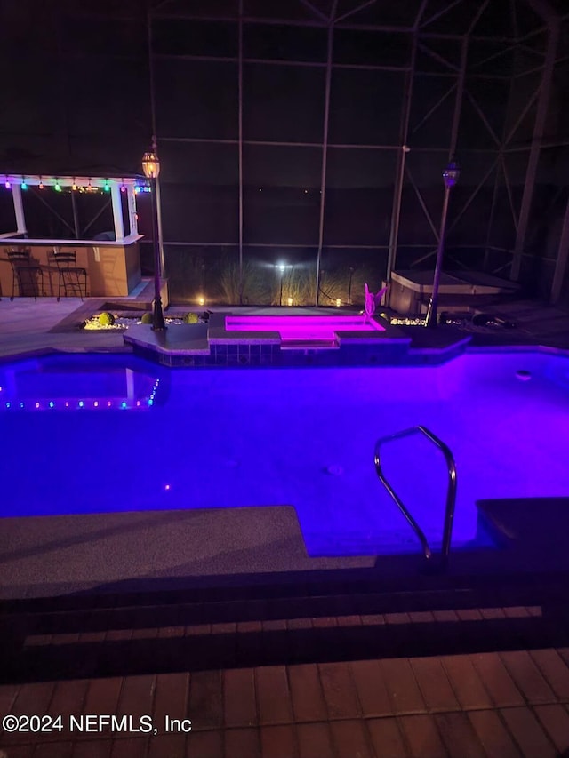 pool at night with outdoor dry bar and a hot tub