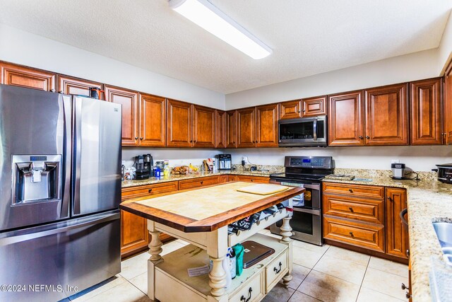 kitchen featuring a textured ceiling, stainless steel appliances, light tile patterned floors, and light stone countertops