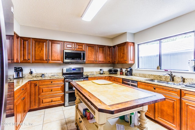 kitchen with appliances with stainless steel finishes, light stone counters, a textured ceiling, and light tile patterned floors