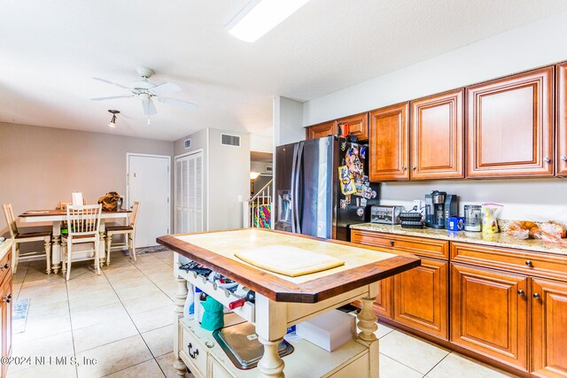 kitchen with light tile patterned flooring, stainless steel fridge, light stone counters, and ceiling fan