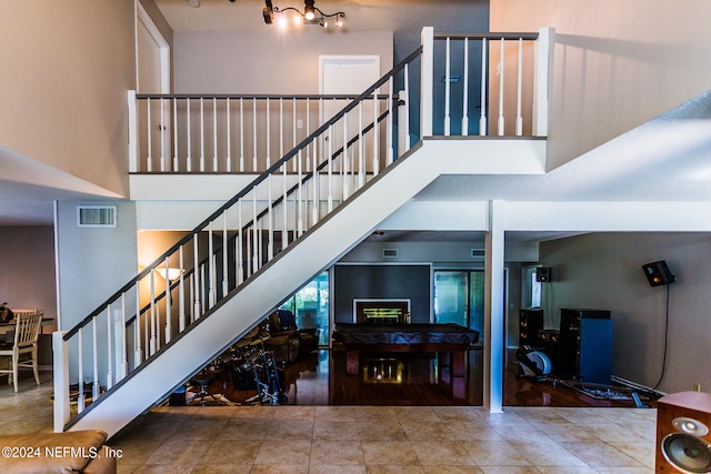 stairway with hardwood / wood-style floors, rail lighting, and a towering ceiling