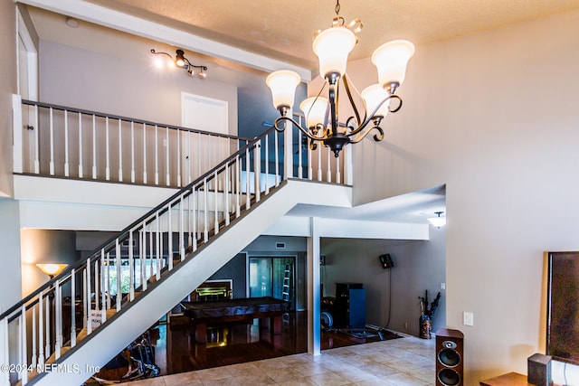 staircase with a towering ceiling, wood-type flooring, track lighting, and an inviting chandelier