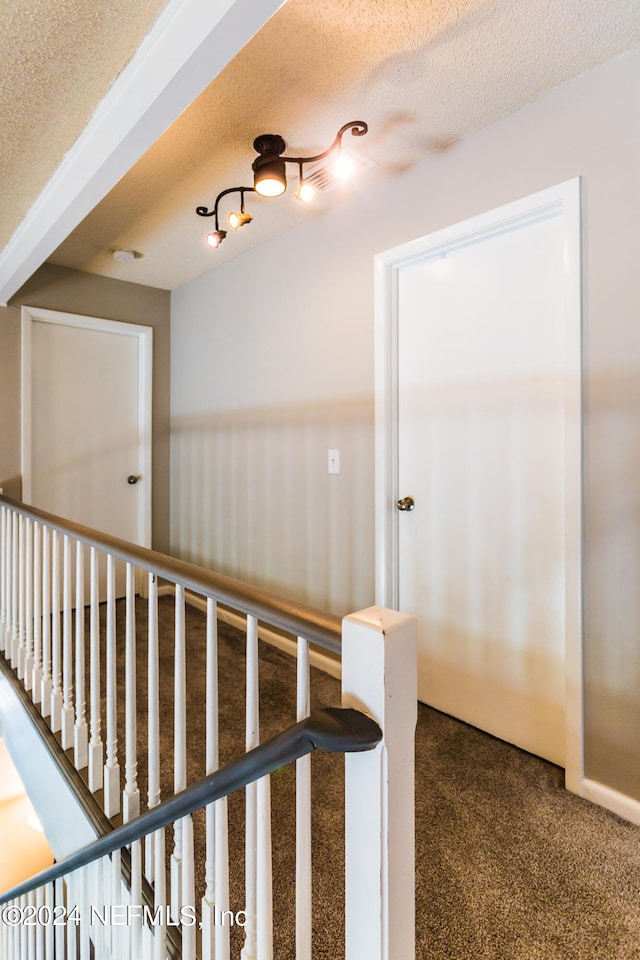 corridor with a textured ceiling, carpet flooring, and track lighting