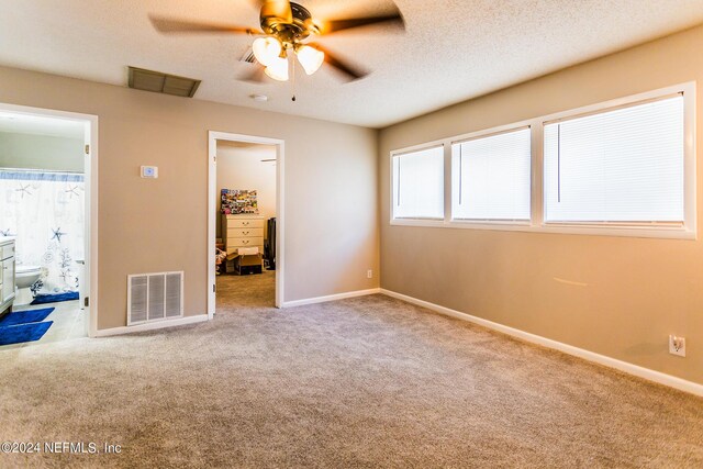 unfurnished bedroom with a textured ceiling, a walk in closet, light colored carpet, and ensuite bath