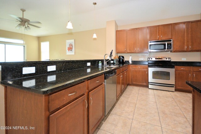 kitchen featuring sink, light tile patterned floors, appliances with stainless steel finishes, pendant lighting, and dark stone counters