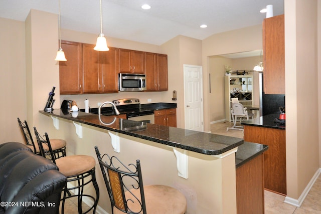 kitchen with dark stone countertops, appliances with stainless steel finishes, a kitchen breakfast bar, kitchen peninsula, and pendant lighting