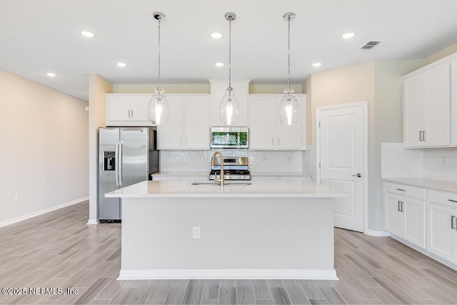 kitchen featuring stainless steel appliances, white cabinets, hanging light fixtures, and an island with sink