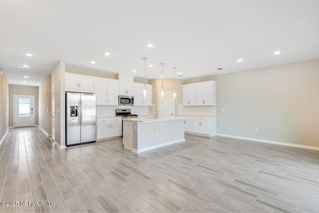 kitchen with appliances with stainless steel finishes, pendant lighting, white cabinets, and an island with sink