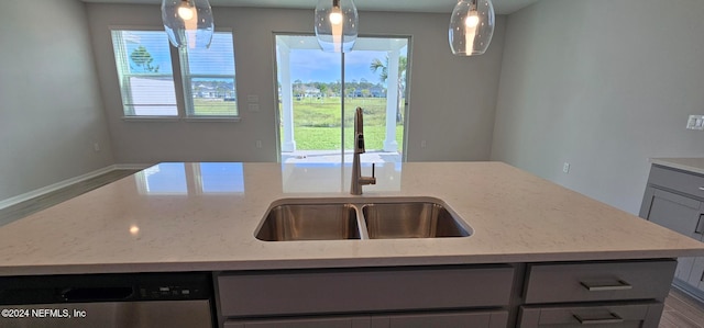 kitchen with a kitchen island with sink, decorative light fixtures, sink, and light stone counters