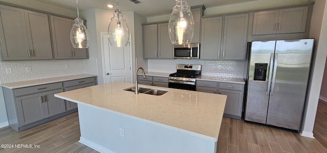 kitchen with sink, appliances with stainless steel finishes, a kitchen island with sink, gray cabinetry, and light stone counters