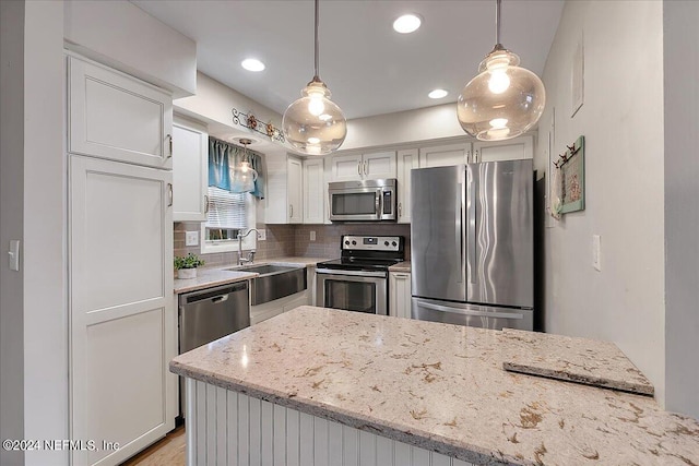 kitchen featuring pendant lighting, sink, appliances with stainless steel finishes, light stone counters, and white cabinetry