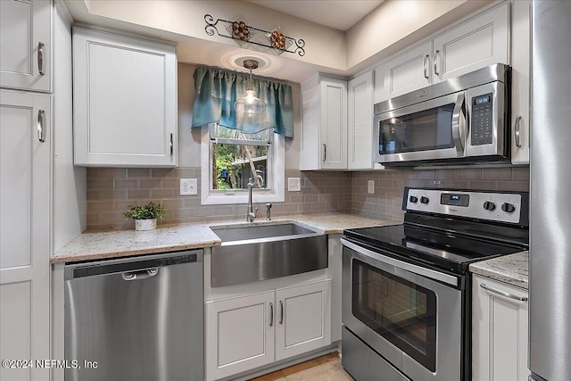 kitchen featuring sink, hanging light fixtures, light stone countertops, appliances with stainless steel finishes, and white cabinetry