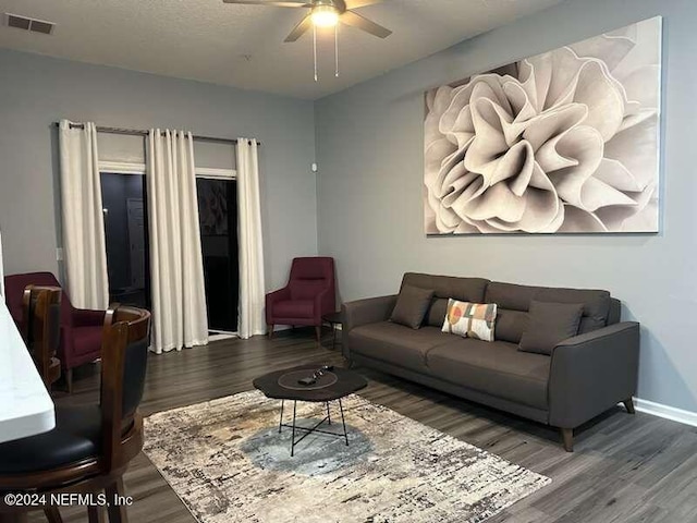 living room with dark wood-type flooring, a textured ceiling, and ceiling fan