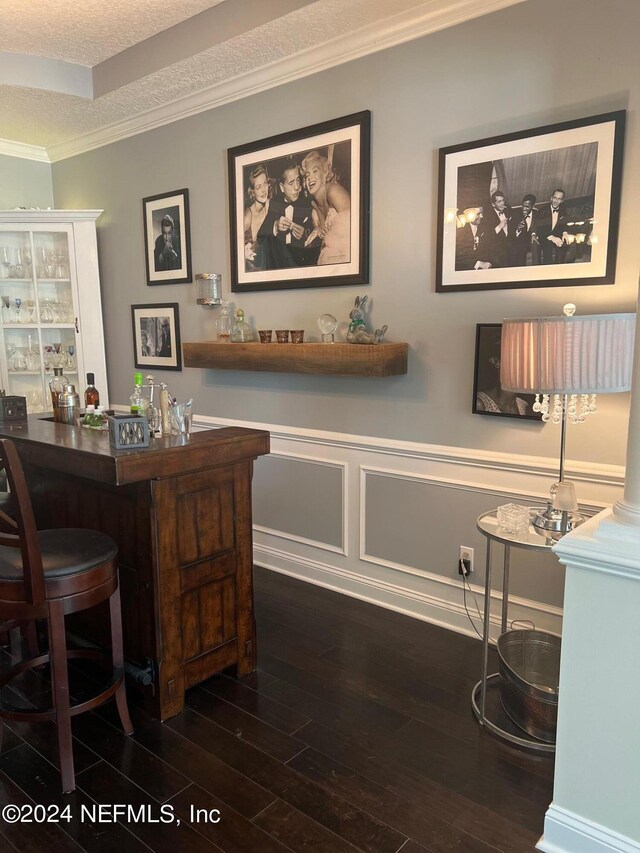 office area featuring indoor bar, a textured ceiling, dark wood-type flooring, decorative columns, and crown molding