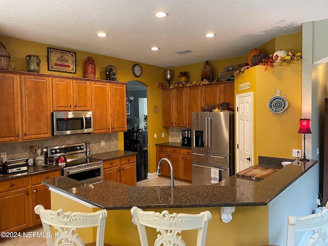 kitchen with sink, kitchen peninsula, a textured ceiling, stainless steel appliances, and a kitchen bar