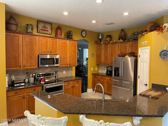 kitchen with appliances with stainless steel finishes, a kitchen bar, a kitchen island with sink, and a textured ceiling