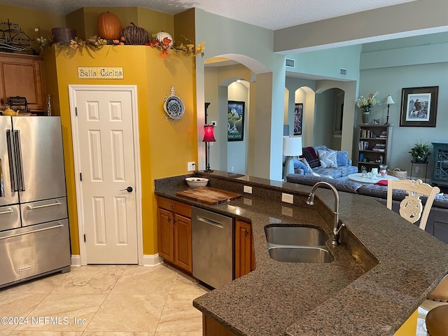 kitchen featuring sink, a textured ceiling, appliances with stainless steel finishes, dark stone countertops, and a kitchen bar