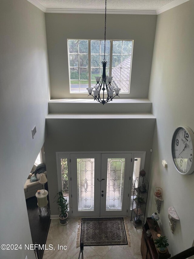 foyer entrance with plenty of natural light, ornamental molding, a notable chandelier, and light tile patterned floors