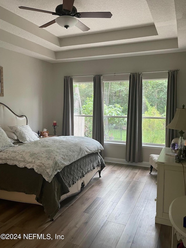 bedroom with a raised ceiling, light hardwood / wood-style floors, and ceiling fan