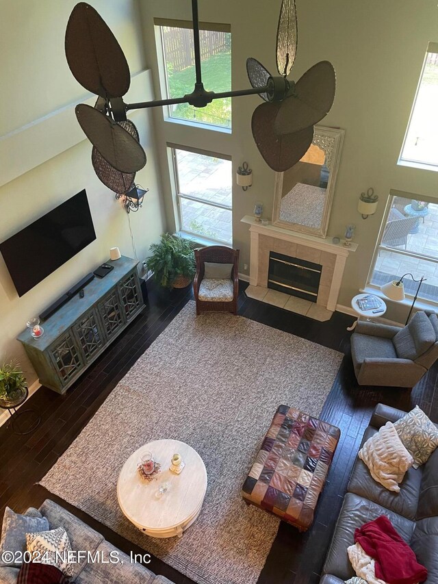 living room featuring dark hardwood / wood-style floors, a tiled fireplace, a high ceiling, and ceiling fan