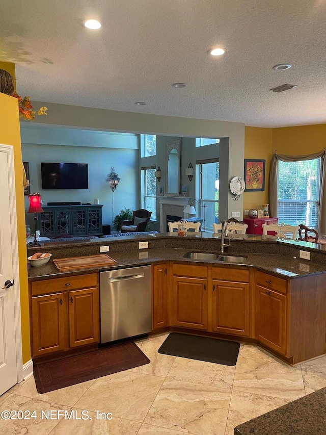 kitchen featuring sink, stainless steel dishwasher, a textured ceiling, dark stone counters, and a fireplace