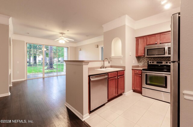 kitchen with appliances with stainless steel finishes, light wood-type flooring, ceiling fan, sink, and tasteful backsplash