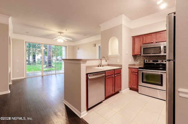 kitchen featuring stainless steel appliances, backsplash, ornamental molding, a sink, and a peninsula