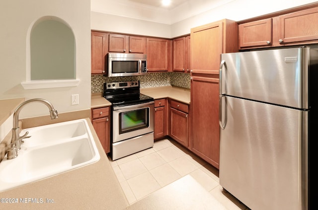 kitchen featuring brown cabinets, stainless steel appliances, backsplash, light tile patterned flooring, and a sink