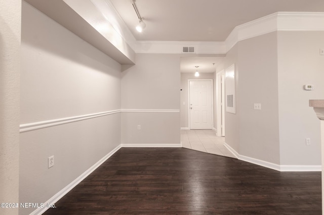 empty room featuring wood finished floors, visible vents, baseboards, ornamental molding, and track lighting