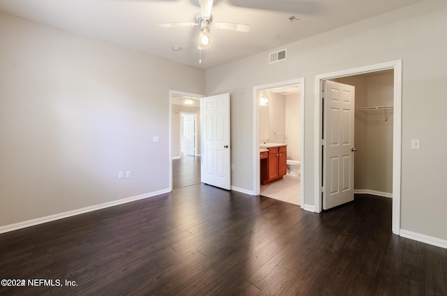 unfurnished bedroom with connected bathroom, wood finished floors, visible vents, baseboards, and a walk in closet