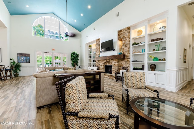 living room featuring built in shelves, a wainscoted wall, a decorative wall, a stone fireplace, and wood finished floors