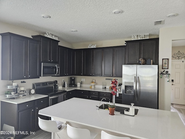 kitchen with a breakfast bar, stainless steel appliances, light countertops, visible vents, and dark cabinetry