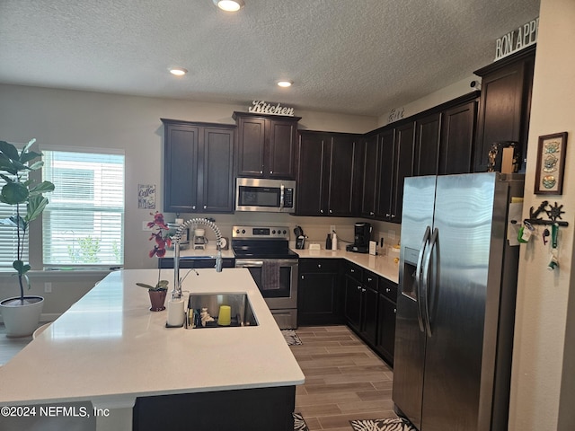 kitchen featuring an island with sink, appliances with stainless steel finishes, wood tiled floor, light countertops, and a sink