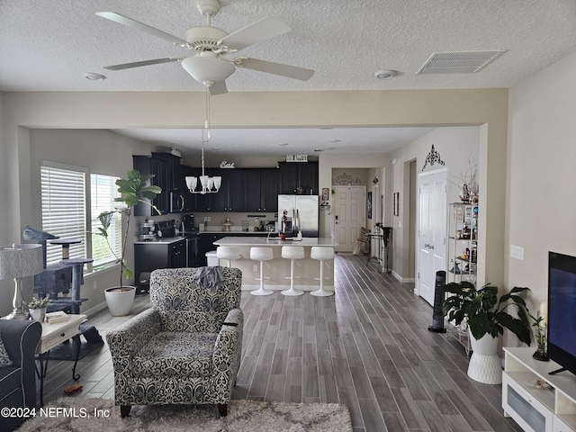 living area featuring ceiling fan, a textured ceiling, visible vents, baseboards, and wood tiled floor