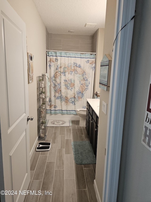 bathroom featuring a textured ceiling, toilet, vanity, shower / tub combo with curtain, and wood tiled floor