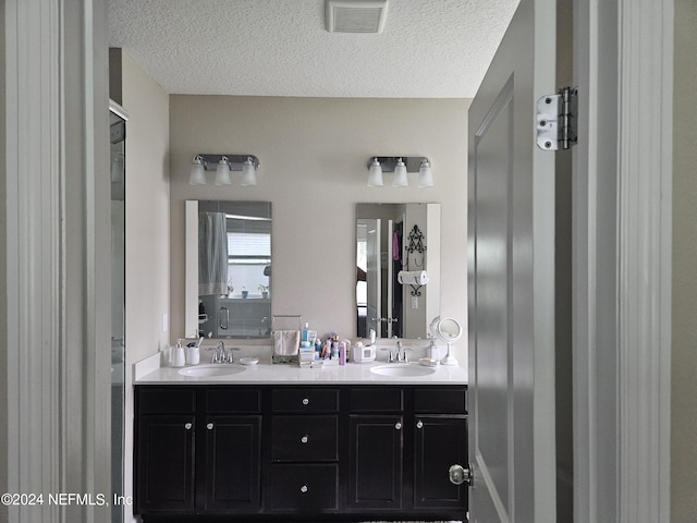 full bath with double vanity, a textured ceiling, visible vents, and a sink